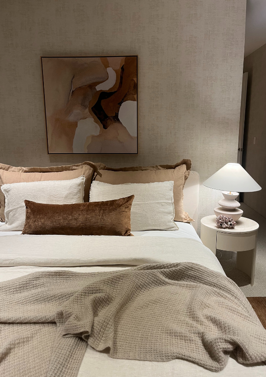 Neatly made bed with decorative pillows and a lamp on a nightstand in a bedroom.