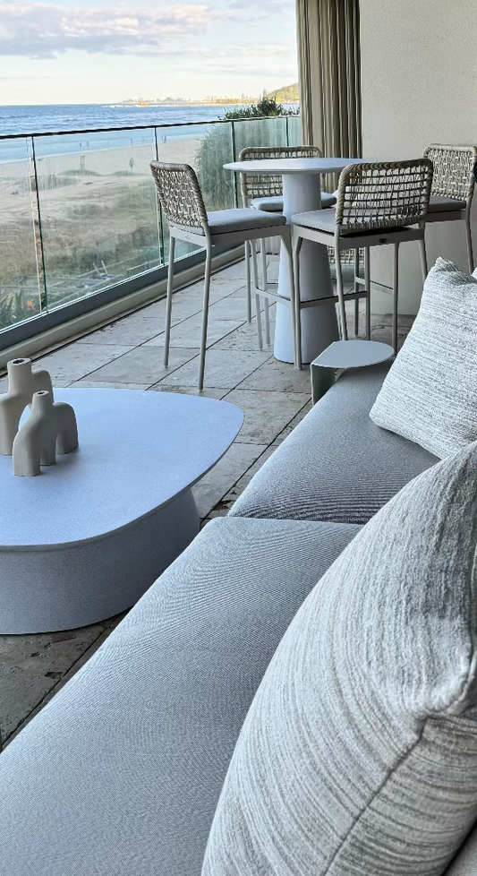 Modern outdoor furniture set with a sofa, coffee table, and chairs on a balcony with ocean view. Bungalow Interiors Gold Coast