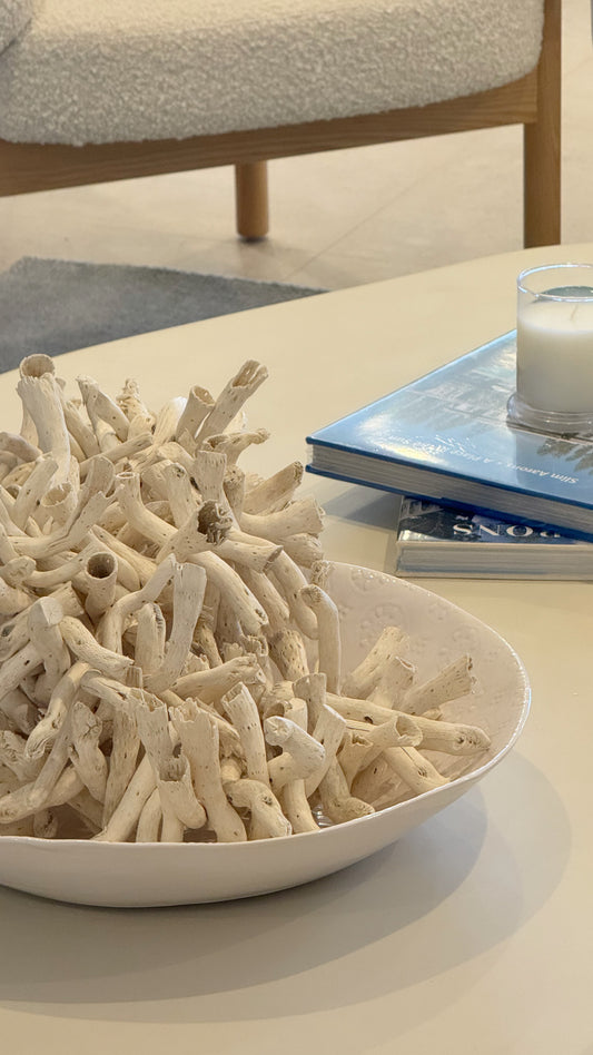 Decorative coral-like sculpture in a white bowl on a table with a candle and book in the background. Bungalow Interiors