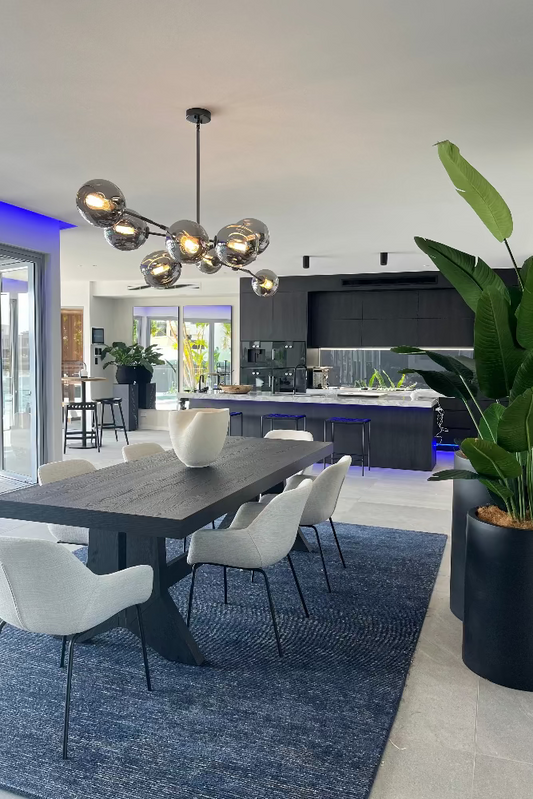 Modern kitchen with dining area featuring a table, chairs, and decorative plants. Bungalow Interiors Design + Home Styling Sovereign Island