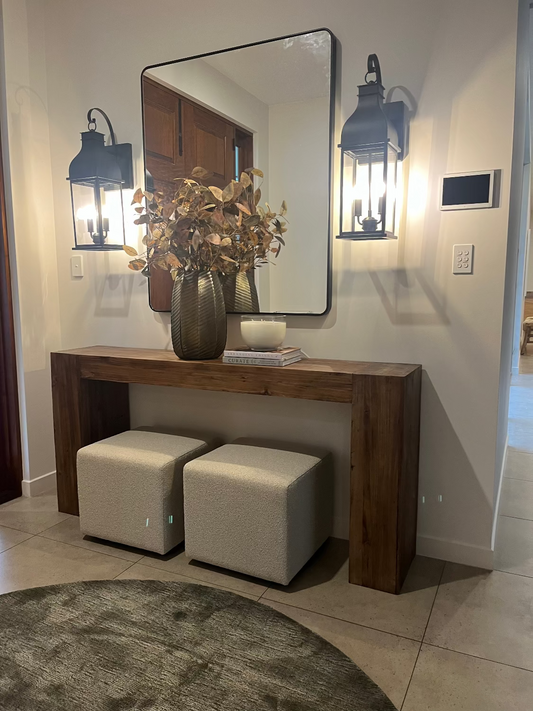 Wooden console table with mirror, decorative items, and stools in a hallway.