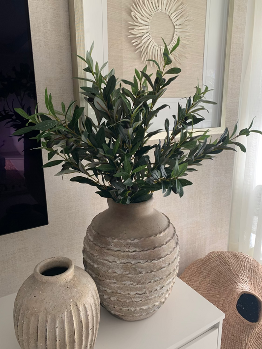 Two textured vases with a plant on a surface, decorative wall art in the background
