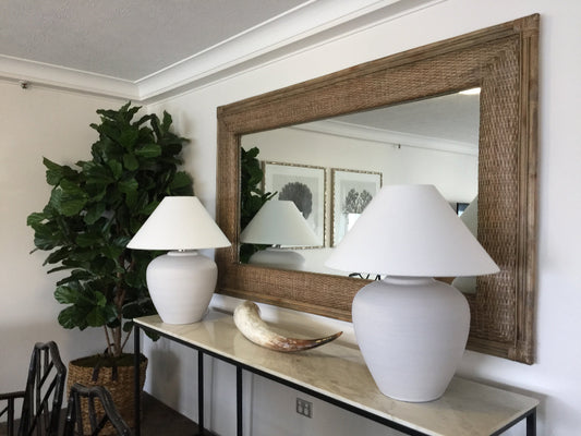 Decorative mirror with wooden frame and white lights on a wall with a plant and shelf in the background.