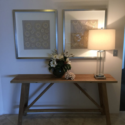 Two framed artworks on a wall with a lamp and decorative plant.