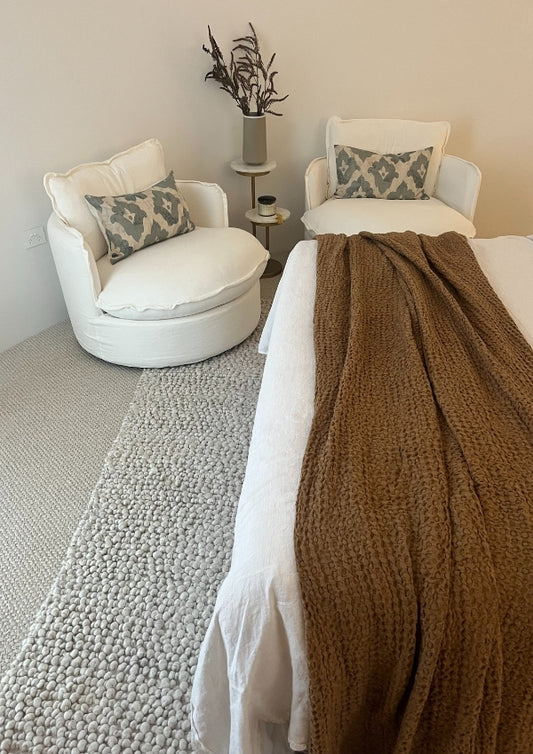 Cozy bedroom with white chairs, a bed with a brown throw blanket, and decorative pillows.