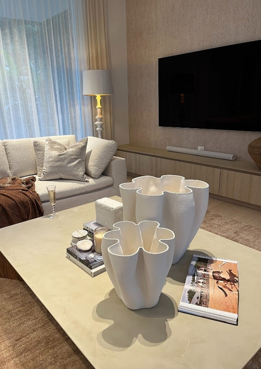 Modern living room with white floral vases on a coffee table, TV, and lamp.