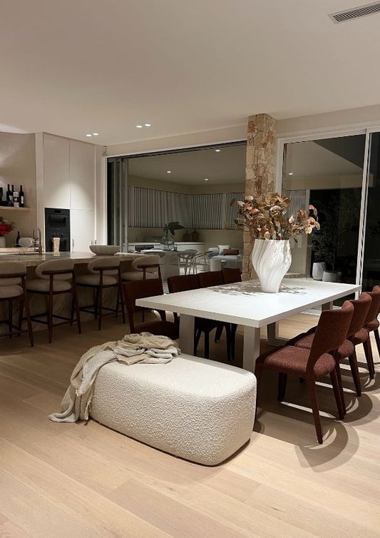 Modern dining room with a white table and chairs, featuring a textured ottoman and decorative elements.