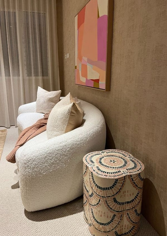 Modern living room with a white curved sofa, decorative pillows, and a colorful abstract painting on the wall.