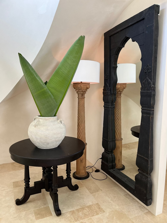 Decorative mirror with intricate design next to a potted plant on a black table.