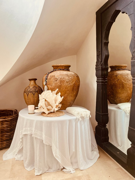 Decorative setting with vases and a shell on a table in a room with a wooden archway.