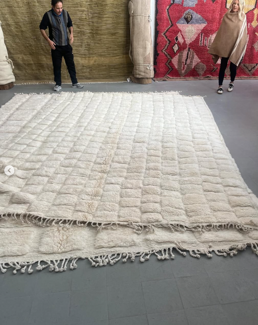 Large beige rug with tassels on a gray floor, with two people standing nearby.