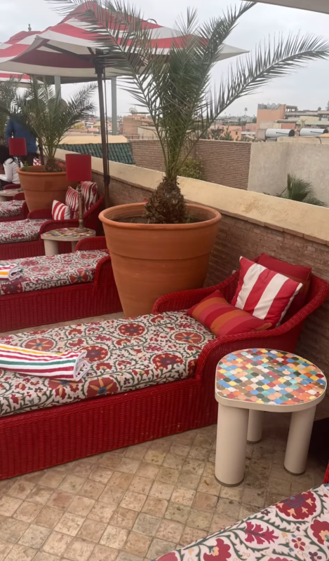Outdoor seating area with red chairs, patterned cushions, and a colorful stool on a tiled patio.