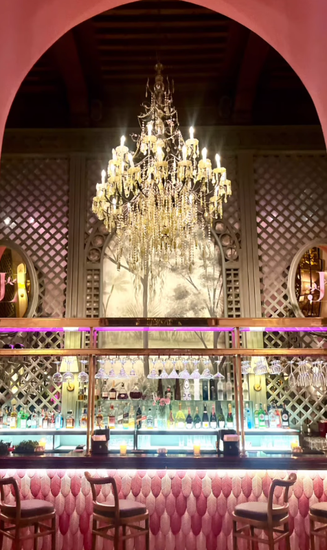 Luxurious bar setting with a chandelier, pink velvet chairs, and decorative walls.