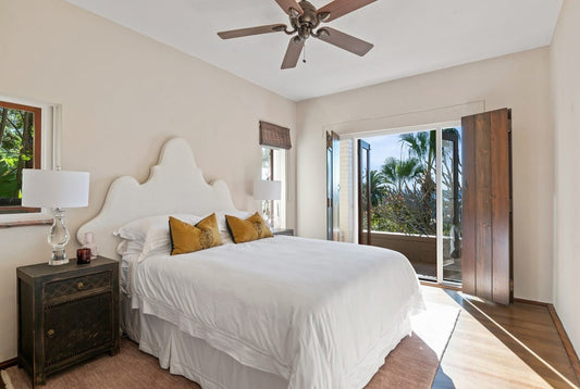Bedroom with a large bed, nightstand, and sliding glass door leading to a balcony with palm trees. Home styling Bungalow Interiors Gold Coast