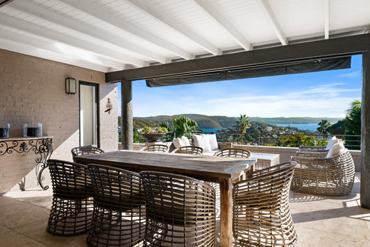 Outdoor patio with wooden table and wicker chairs, overlooking a scenic view.