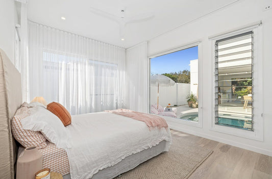 Modern bedroom with a view of a pool area through large windows.  Bungalow Interiors Gold Coast, coastal interior design styling