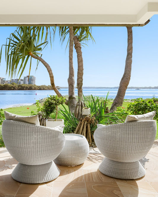 Bungalow Interiors Home Styling.  White outdoor chairs on a patio with a scenic view of water and palm trees.