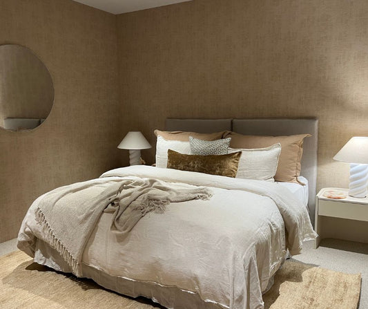 Neatly made bed with beige and brown bedding in a bedroom setting.
