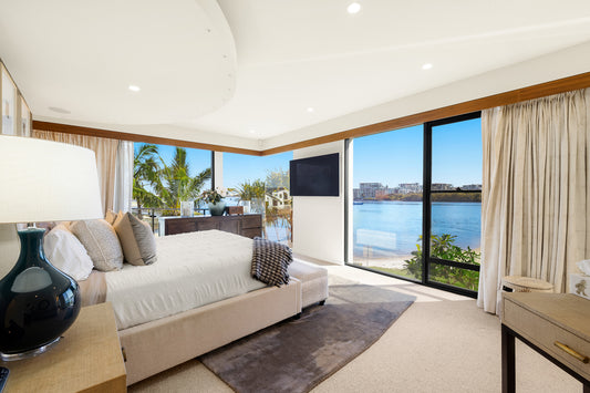 Modern bedroom with a large window view of water and palm trees.  Bungalow Interiors, home styling Gold Coast