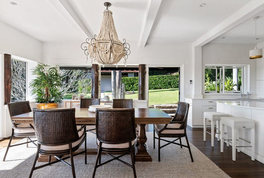 Dining room with wooden table and chairs, chandelier, and large windows. Home styling Bungalow Interiors Gold Coast